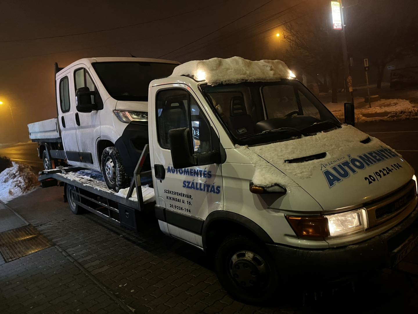 Auszmann teherautó havas, ködös éjszakán autót szállít
